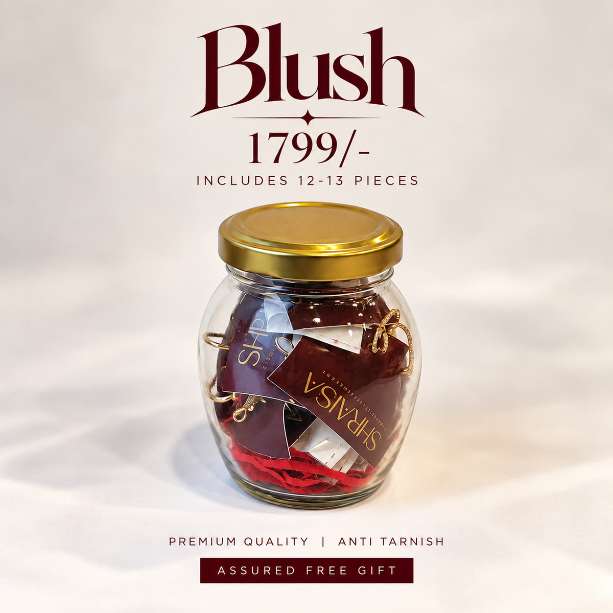 A clear glass jar with a gold lid containing red and burgundy gift tags inside, set against a plain white background with text reading 'Blush 1799/-' and 'Includes 12-13 pieces'.